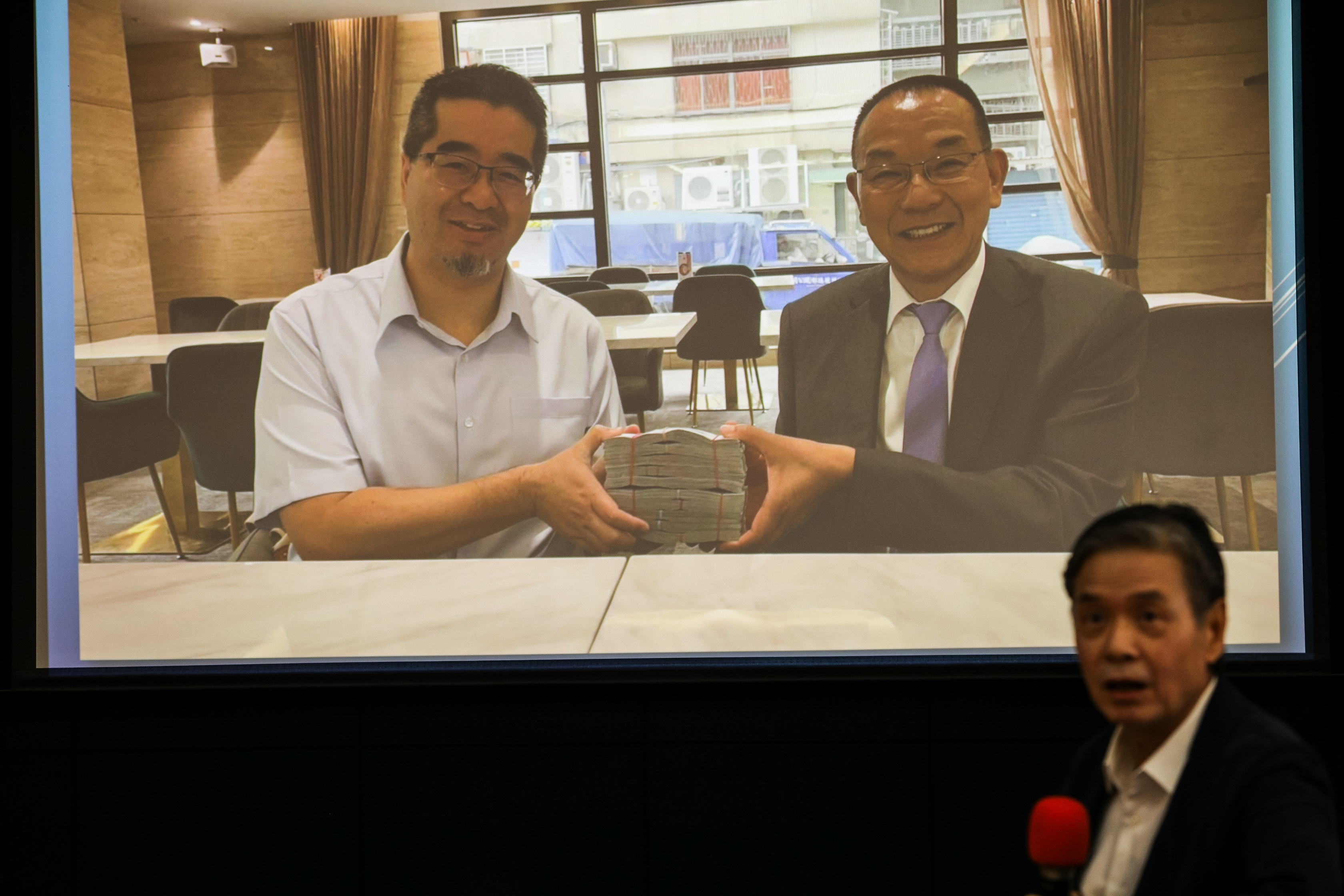 金溥聰拿出照片,畫面可見蕭旭岑與廈門台協會長韓螢煥合捧現金。(鏡報鄒保祥)