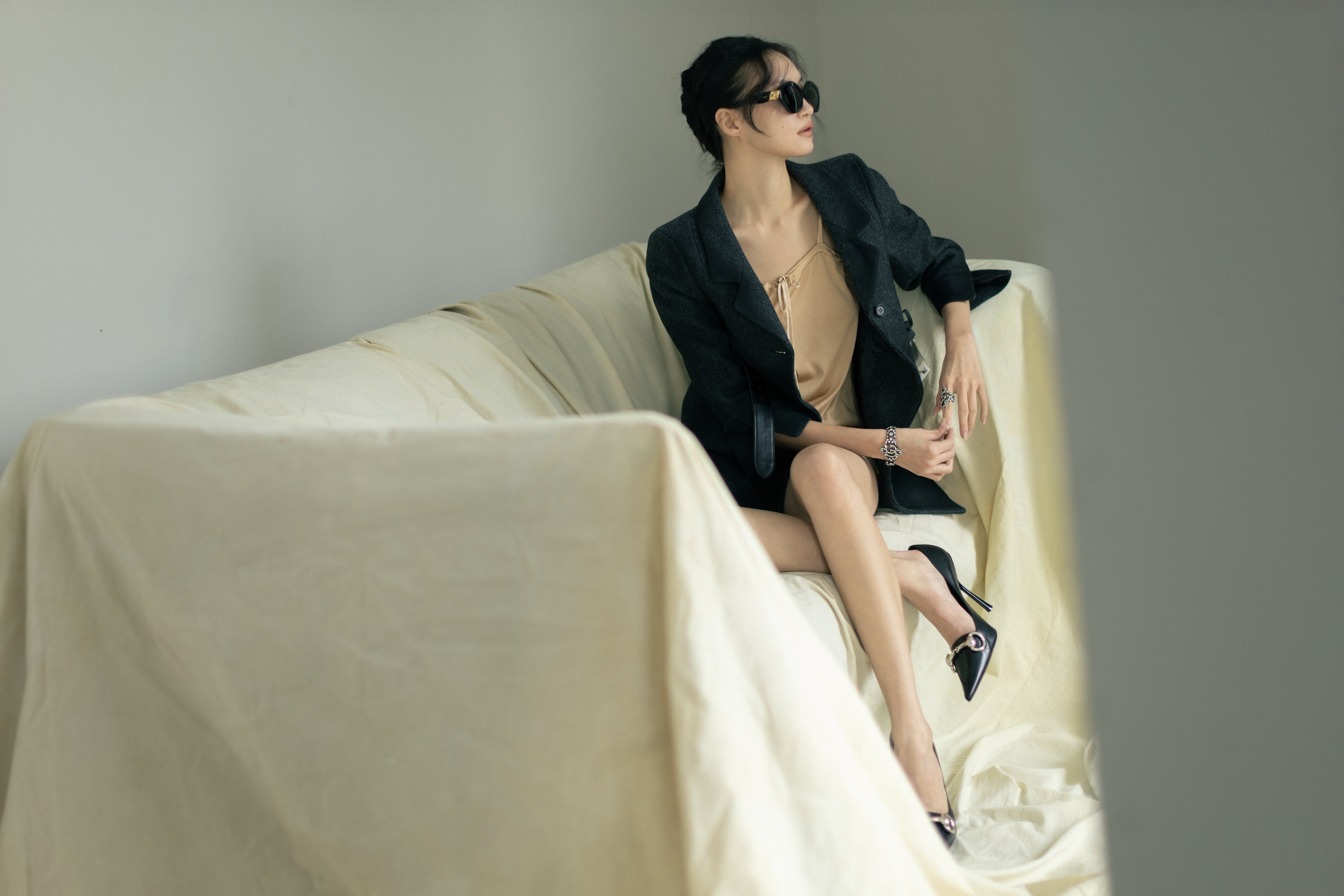 膚色內裡綁帶洋裝 價格店洽 by MIU MIU;灰色造型外套 價格店洽 by MIU MIU;黑色高跟鞋 價格店洽 by GUCCI;黑色墨鏡 NT$14,250 by LOEWE;水晶裝飾戒指 價格店洽 by GUCCI;水晶裝飾手鍊 價格店洽 by GUCCI。