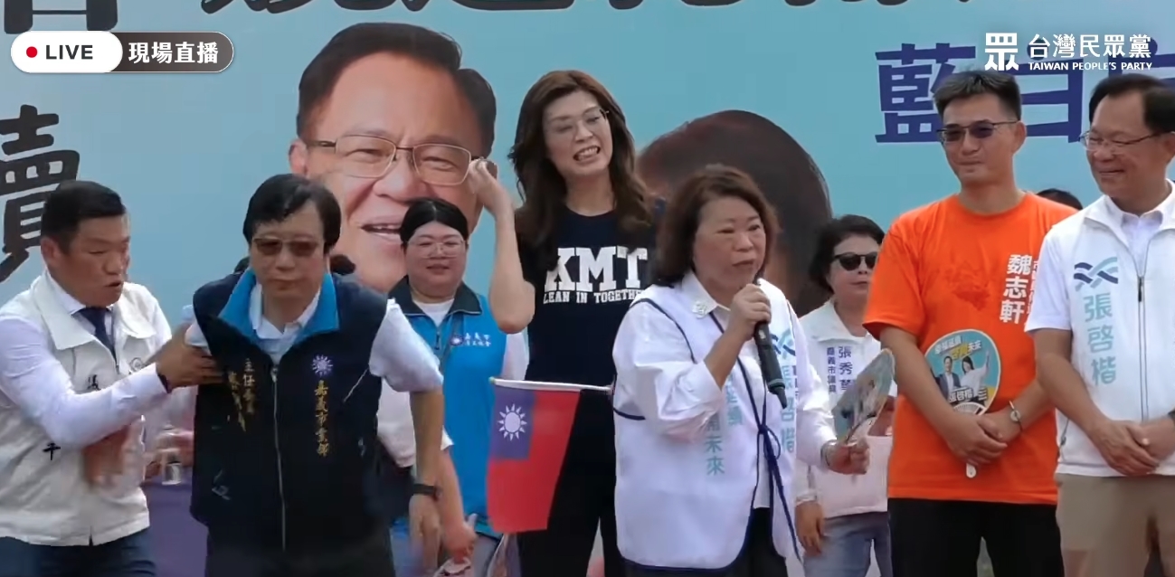 國民黨嘉義市黨部主委兼競總執行總幹事蔡明顯(左二)突然感到暈眩、重心不穩跌落舞台。(翻攝自民眾之聲YT)