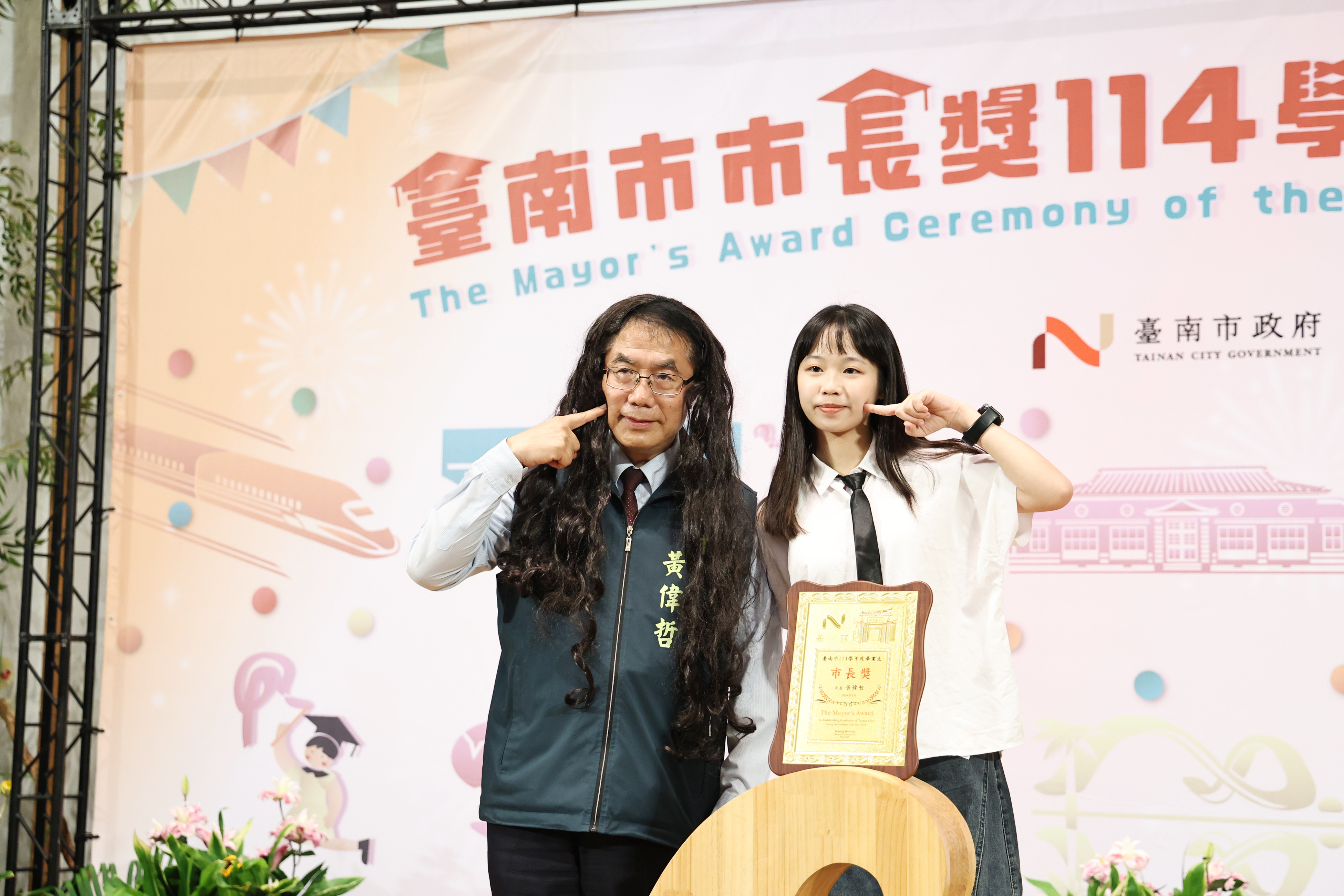 台南市長黃偉哲對於畢業生合照要求幾乎有求必應,戴浪漫長捲髮也秒答應。(台南市政府提供)